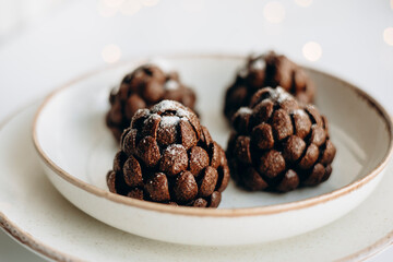Chocolate pine cone dessert with powdered sugar on ceramic plate.