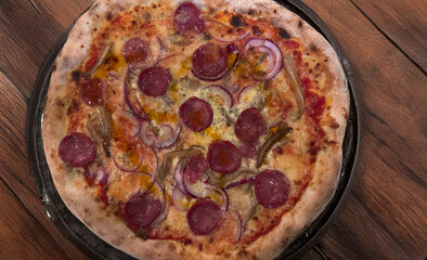 Spicy sausage pizza with red onion and melted cheese on wooden table