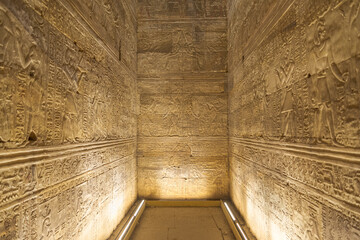Internal room with dim light at the famous Edfu temple, dedicated to the god Horus. High walls are full of hieroglyphics.