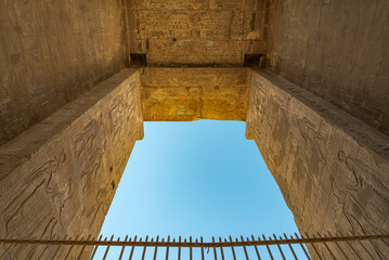View from the bottom to the top of the main entrance gate of the temple of Edfu, Egypt, dedicated to the god Horus. Iron fence at the bottom. With blue sky.