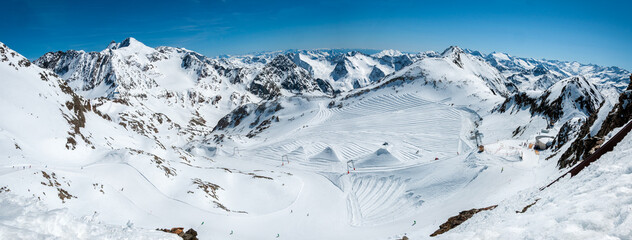 Stubai glacier in Austrian Alps with ski slopes, ski tow, upper station, skiers and snowboarders,  View from Schaufelspitze. Panorama of Stubai Alps. Quasi-terraced slopes covered against melting