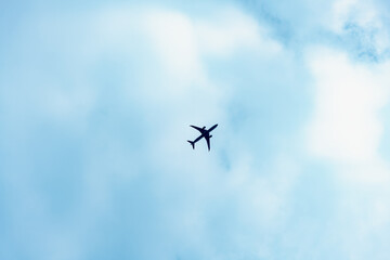 Silhouette of an airplane flying diagonally across a clear blue daytime sky, captured directly overhead. Minimal scene emphasizing motion and geometry in bright natural light.