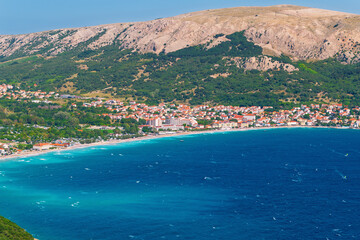 Obraz premium Coastal town with red roofs nestled between mountains and clear blue sea. Baška, Krk island, Croatia