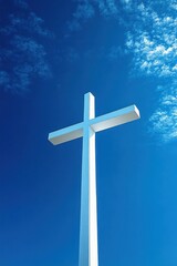 Tall white cross towering against a vibrant blue sky with scattered white clouds, symbolizing faith and hope