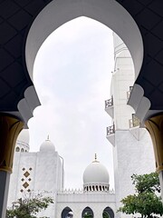 White mosque domes and minaret framed through an elegant Islamic archway. A peaceful architectural composition symbolizing beauty, spirituality, and cultural heritage.