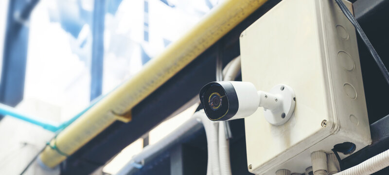 A modern white CCTV security camera mounted outdoors on a building with an electrical box, representing surveillance, protection, and modern technology.