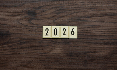 The year 2026 spelled out using retro-style number tiles centered on a dark wooden surface, symbolizing the upcoming new year.