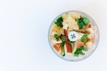 Top-down view of a blender filled with fruits and greens for a smoothie, against a white background. Empty space on the side is perfect for adding text.