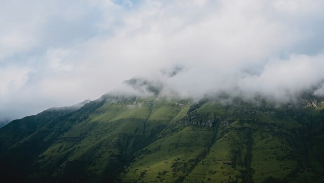 Clouds envelop the summits of a verdant mountain, seasonal change