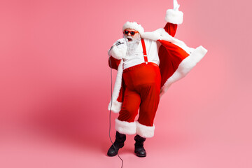 Santa performs on pink backdrop wearing red suit cape and hat singing into a microphone for festive...