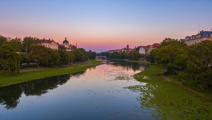 Obraz premium A river scene bordered by trees and distant buildings, seasonal change