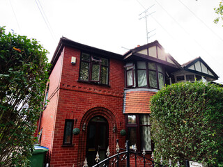 Red brick house with bay windows in Manchester, UK, surrounded by a hedge and decorative fence