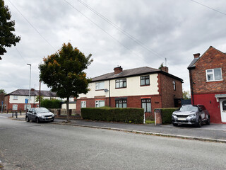 Residential street in Manchester with brick houses and parked cars under a cloudy sky