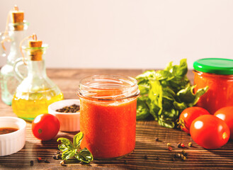 Homemade tomato sauce in glass jar with herbs and tomatoes nearby.