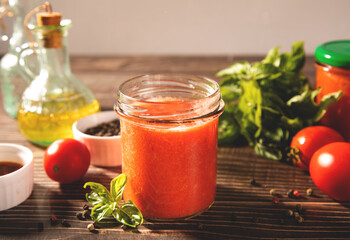Homemade tomato sauce in glass jar with herbs and tomatoes nearby.