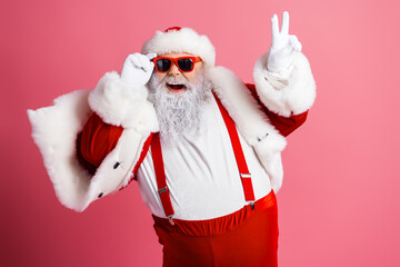 Joyful Santa in red suit with white fur trim posing playfully against pink background