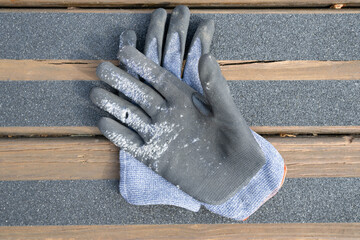 A pair of work gloves with hole, worn from placing anti-slip tape onto a wooden deck ramp.