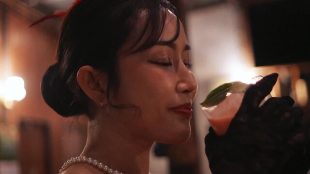Close-up of a stylish Asian woman in retro attire slowly enjoying a cocktail at a dimly lit vintage bar or lounge, capturing a moment of relaxed sophistication at night