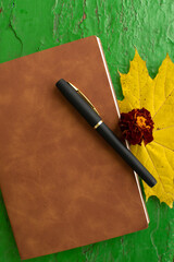 Pen, brown-covered notebook, marigold and yellow maple leaf