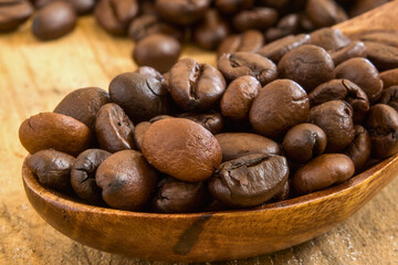 Close up of roasted coffee beans in a wooden spoon on a table