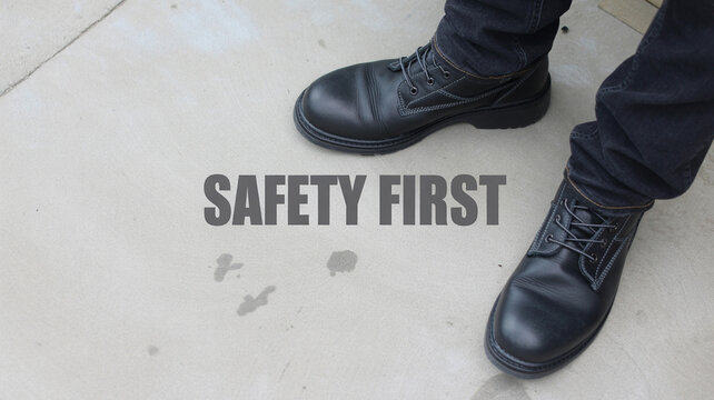 A person wearing black leather safety boots standing on a wet floor with safety first text overlayed