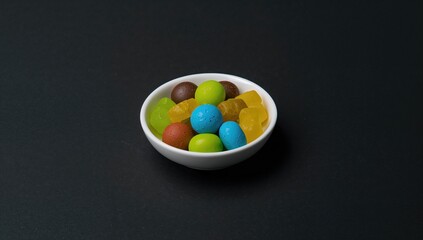 Colorful candies arranged on a small white dish against a dark backdrop, high sugar load