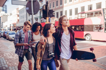 Young adult friends walking with skateboard on city street with red double-decker bus, cheerful