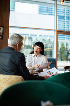 Adult woman and mature man discuss finance in cafe, focused