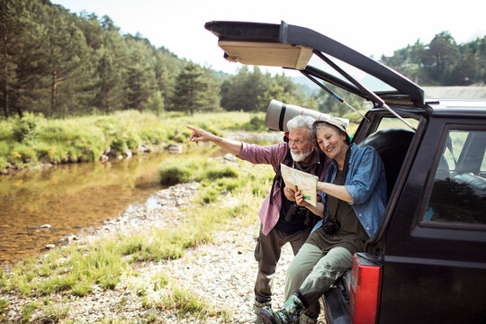 Senior couple smiling and pointing with map by forest river