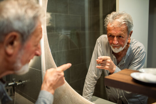 Senior man playfully pointing at his reflection in home bathroom