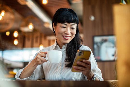 Adult woman smiling with coffee using smartphone at cafe