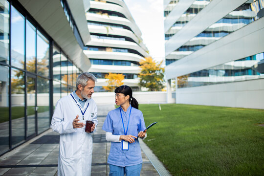 Senior doctor and adult nurse having focused discussion on hospital campus