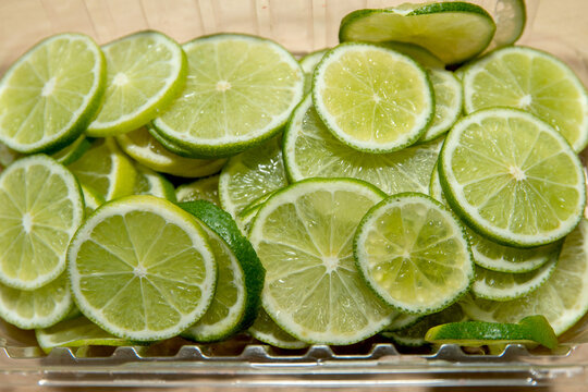 Juicy, fresh lime wedges in a clear container for cocktails or catering. Close-up of freshly cut lime wedges.