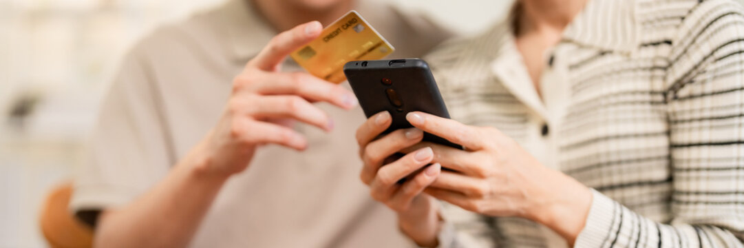 Asian adult couple perform secure online shopping home using mobile phone entering credit card details for convenient digital payment transaction modern lifestyle