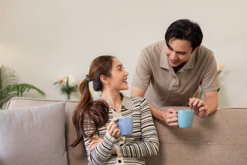 Asian adult couple sharing happy coffee moment on comfortable sofa at modern home living room...