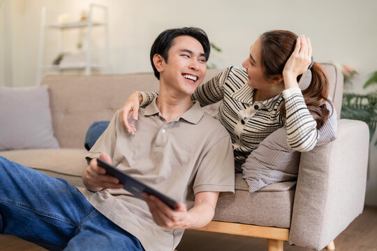 Asian young adult couple relax watch digital tablet happy together home cozy living room enjoy connection leisure weekend life bonding