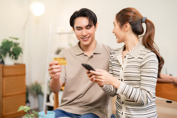 Adult Asian couple online shopping digital payment using smartphone credit card cozy home apartment happy financial transaction modern lifestyle technology banking secure purchase
