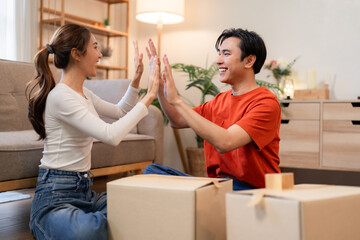 Asian adult couple high five celebrating successful home move unpacking boxes new apartment living room