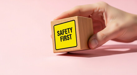 Hand holding a wooden block with safety first message against a pink background in a studio shot
