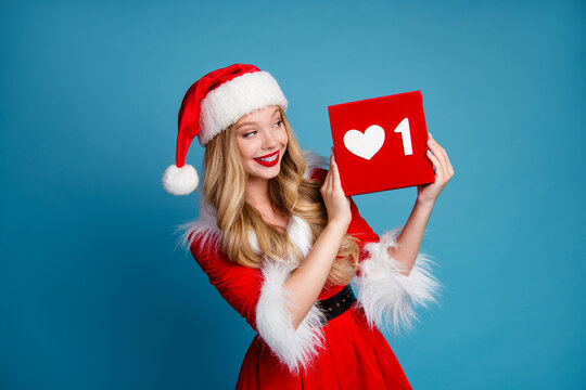 Woman in festive santa dress holding red square with heart and number one against blue background for christmas holiday promo