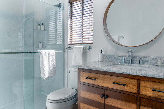 White modern bathroom interior with marble sink, wood cabinet, glass shower