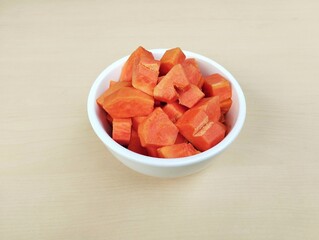 Fresh papaya slices in bowl with wooden table background. High angle view 