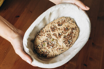 Person holding freshly baked sourdough with seeds in a banneton  