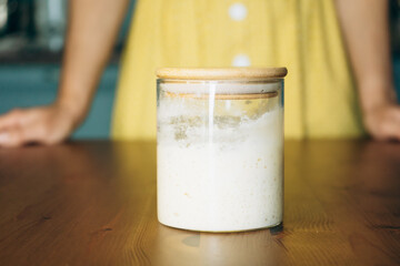 Jar with active sourdough starter on wooden table in kitchen  