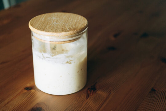 Jar with active sourdough on wooden surface in kitchen setting   - Powered by Adobe