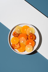 Surtido de rodajas de cítricos peladas en un plato blanco sobre fondo azul y blanco. Vista superior	