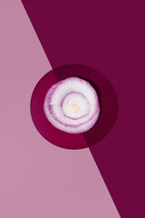 Aros de cebolla roja cruda colocados sobre un fondo rosa y granate. Vista superior
