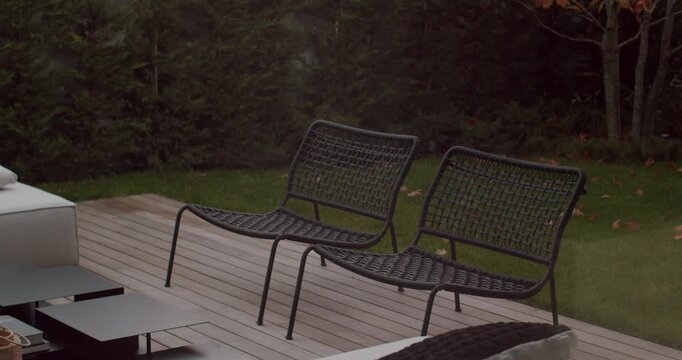Two empty black wicker patio chairs sit on a wooden deck in a backyard. The lush green grass and shrubs create a peaceful atmosphere. Perfect for relaxing.