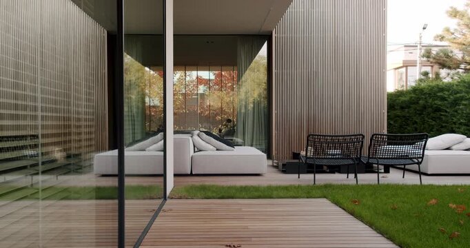 Modern house with garden furniture on a wooden terrace. Cozy outdoor seating area. Large windows and wooden facade. Natural light and comfortable ambiance. relaxation and enjoying the outdoors.