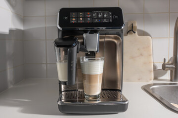 Touchscreen bean-to-cup machine with a finished latte macchiato. Kitchen counter scene, stainless and clean.